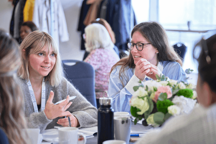 A woman sitting at a round table while other women beside her listen.